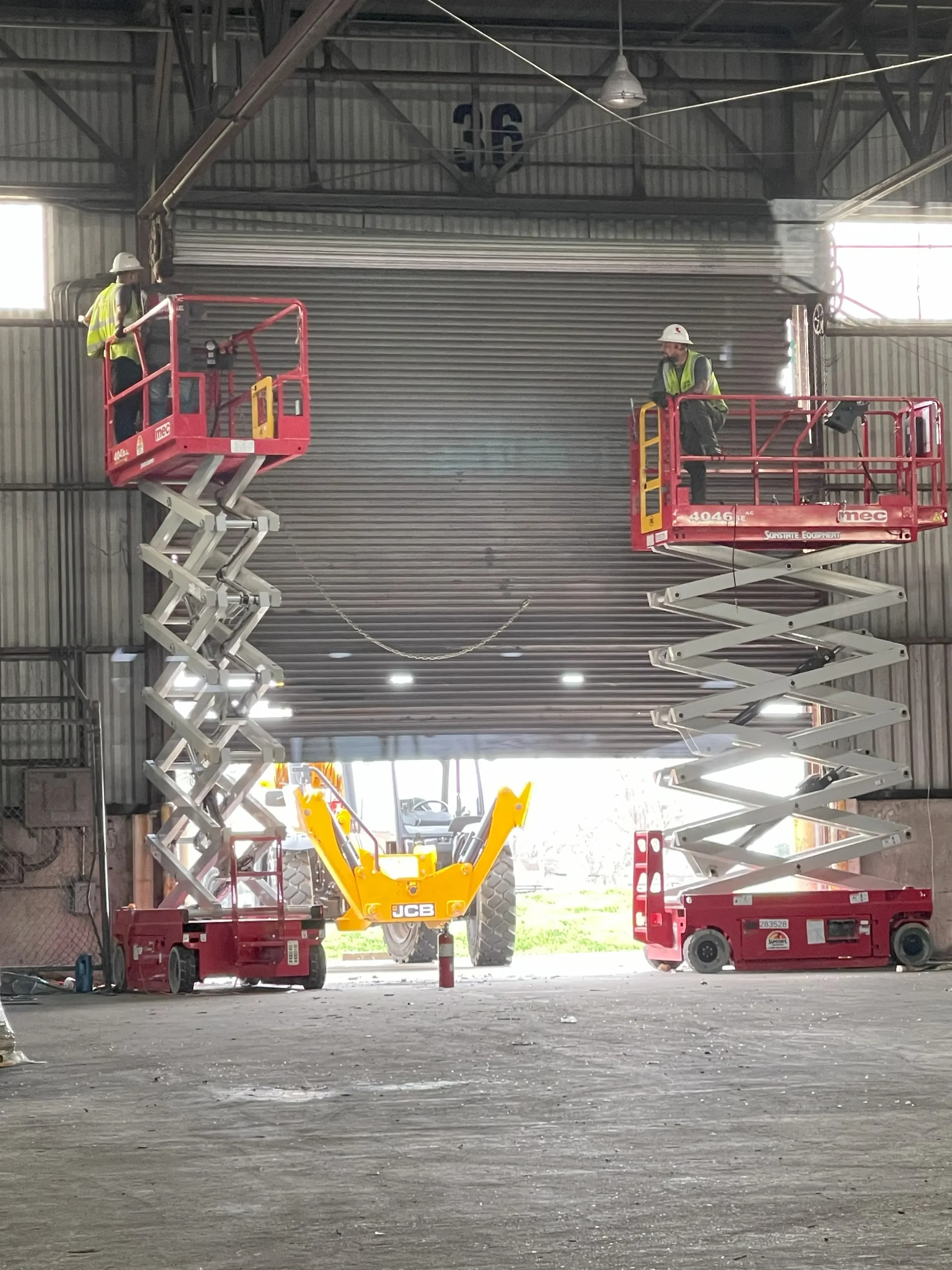 Technicians on scissor lifts servicing a large rolling steel door in a New Orleans warehouse