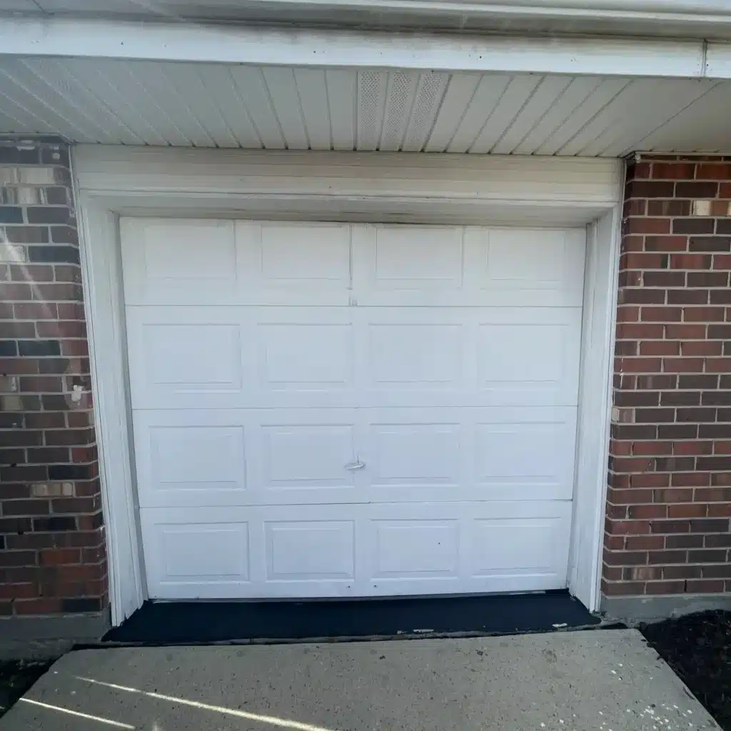 Worn white single-car garage door on a brick home in Kenner before replacement