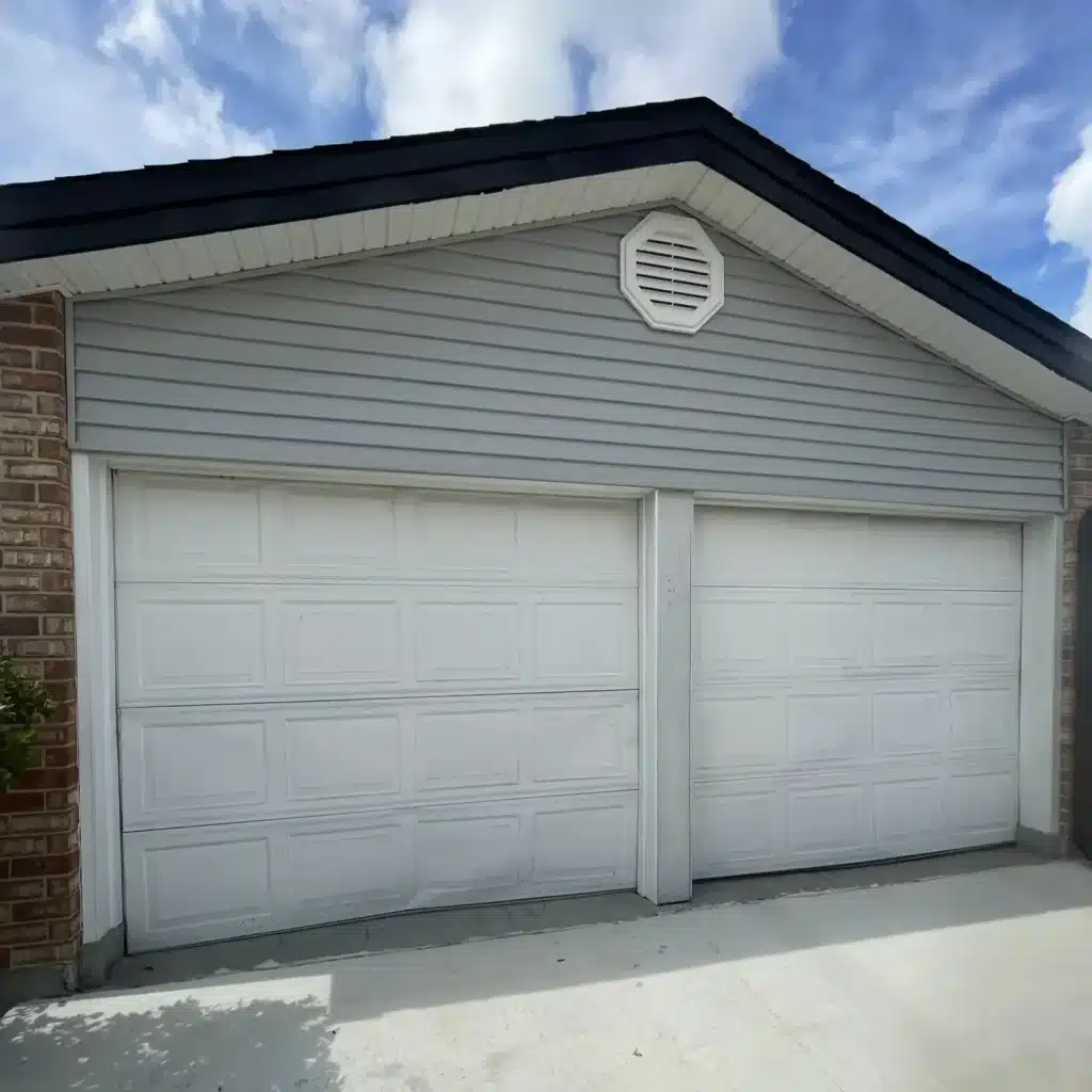 Aging white two-car garage door on a brick home in Metairie before replacement