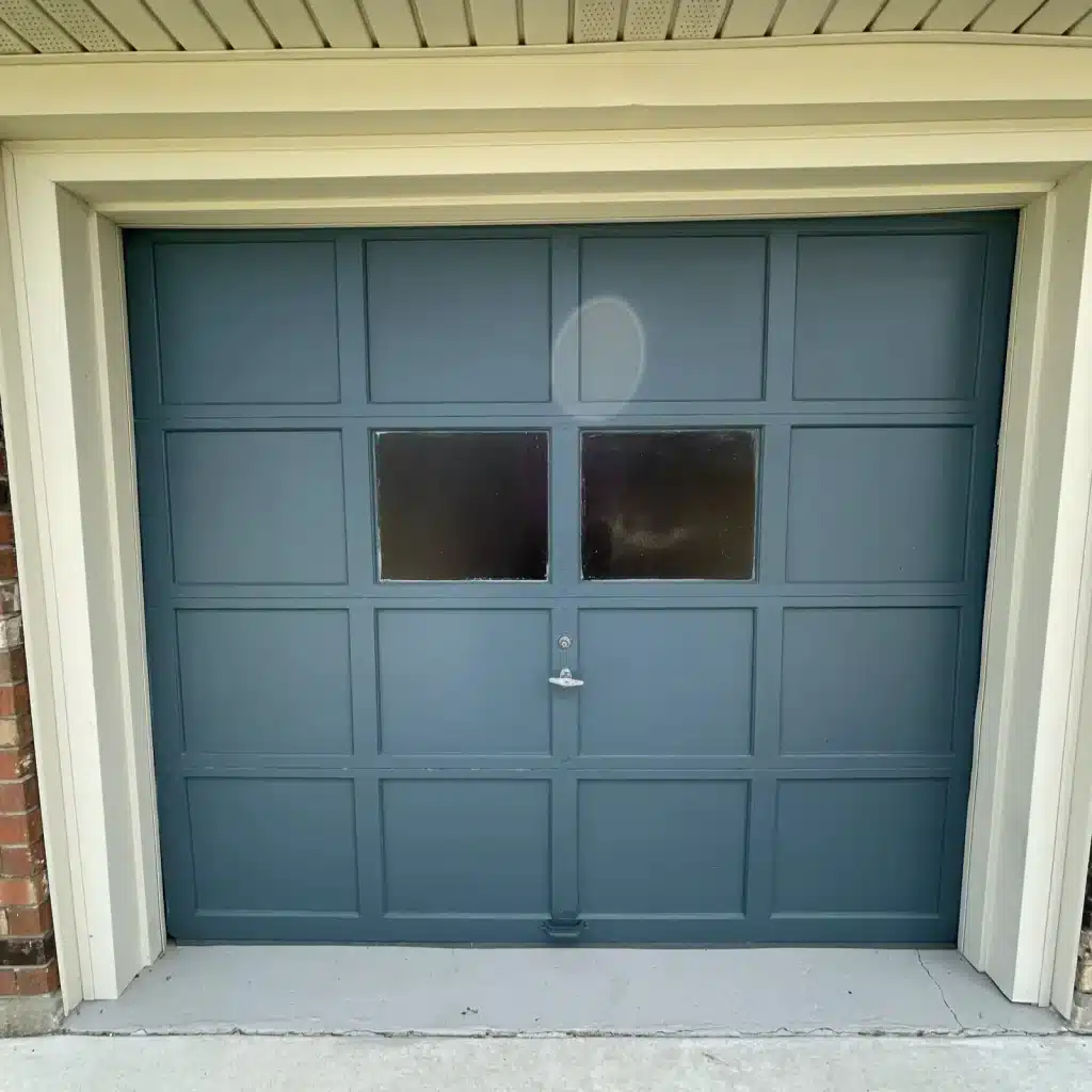 Teal single-car garage door with window panel before replacement — New Orleans brick home