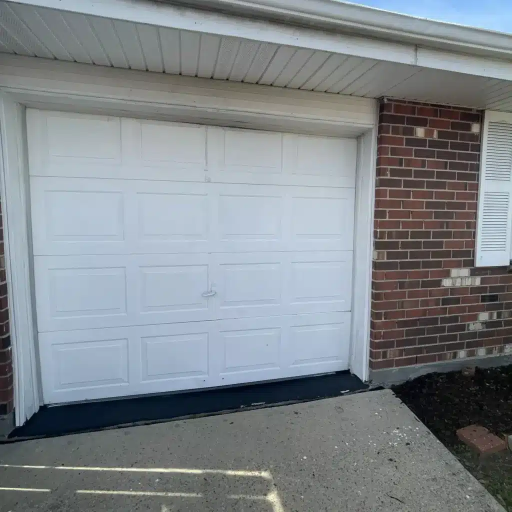 Worn white panel garage door before reinstallation on a River Ridge brick home