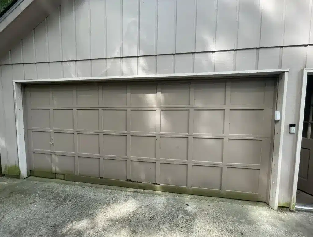 Worn tan two-car garage door with damaged panel before replacement — New Orleans home