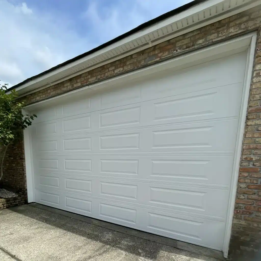 New white raised-panel garage door installed on a Kenner brick home