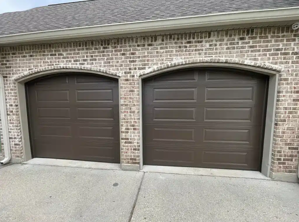 New dark brown garage door with arched trim installed on a New Orleans brick home