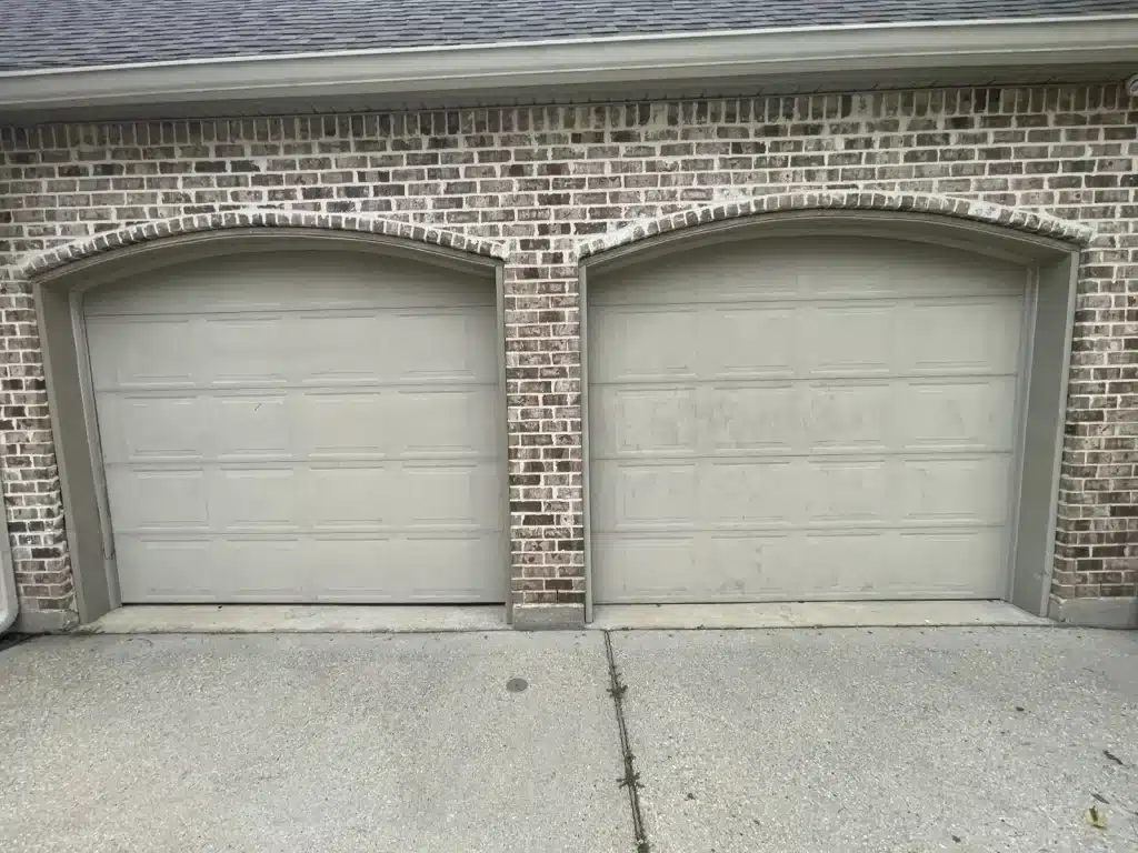Faded single-car garage door with arched trim before replacement on a New Orleans brick home