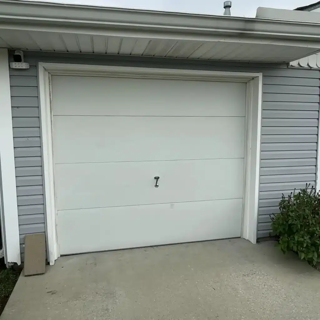 Plain white single-car garage door on a gray sided home in Gretna before upgrade