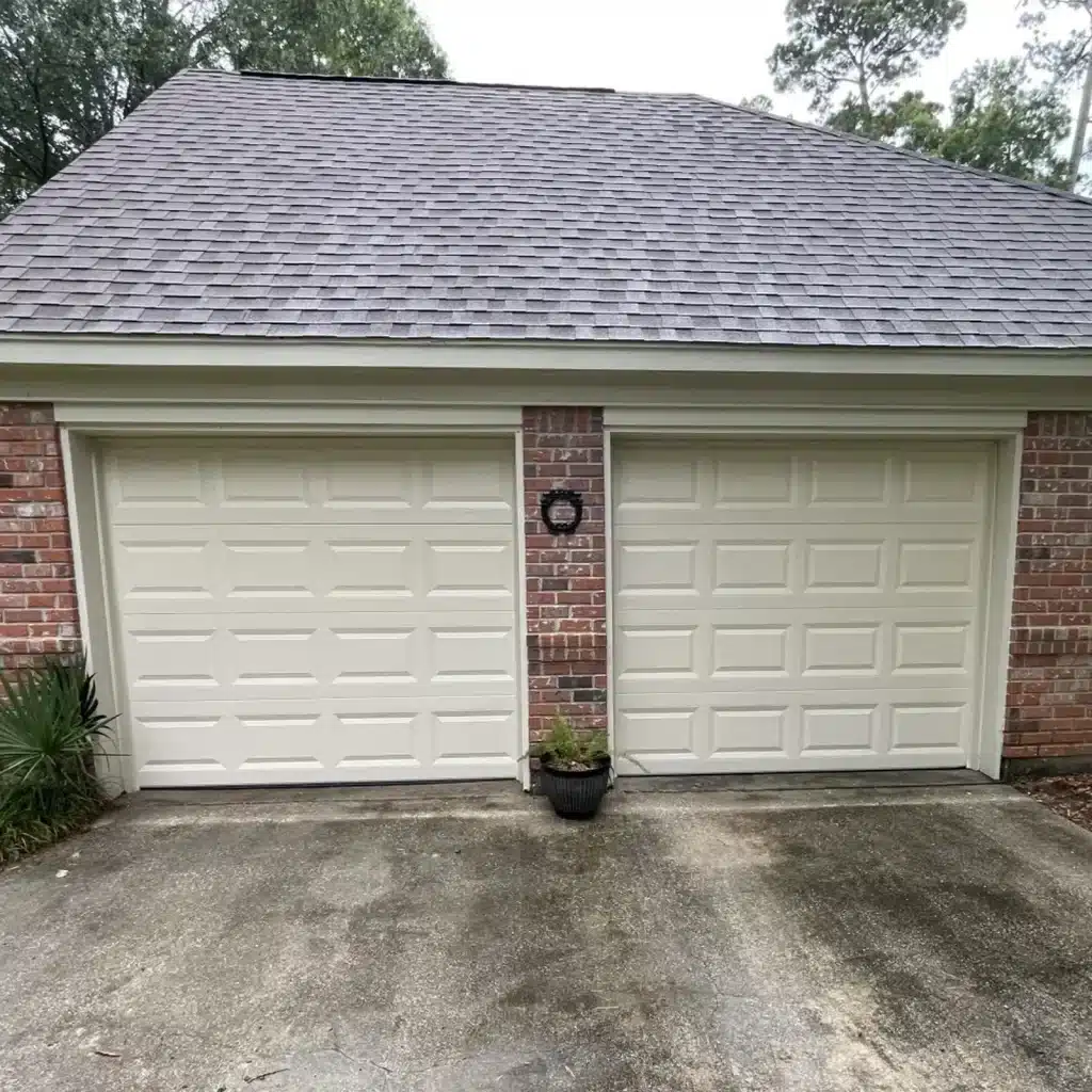 New white raised-panel single-car garage door installed on a Metairie brick home