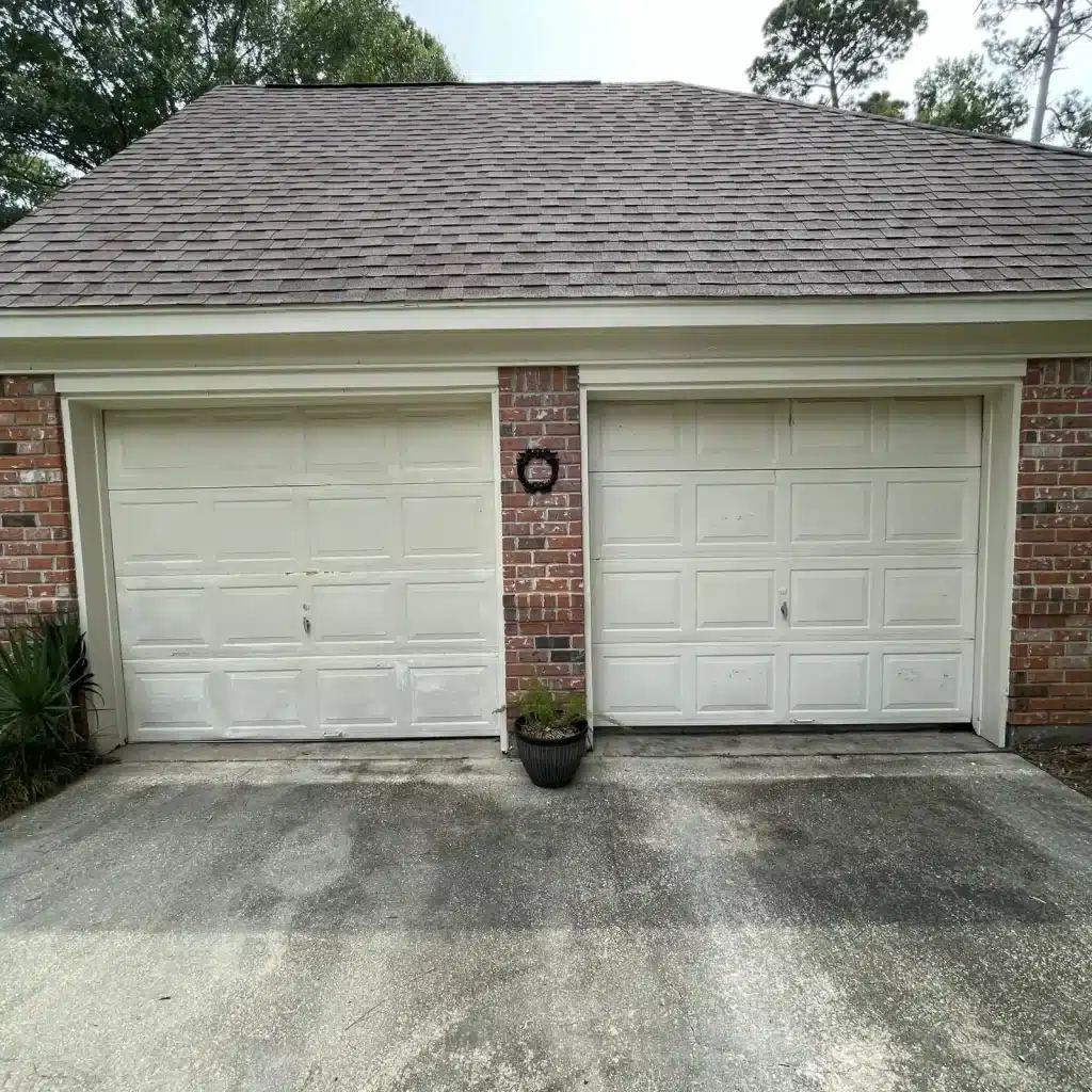 Worn white single-car garage door on a Metairie brick home before replacement